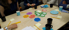 People sitting around a table with papers, pencils, and colorful hexagon cards.