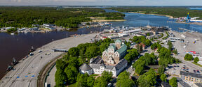Aerial view of Turku Castle surrounded by trees and a port area with ships and parking.