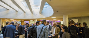 People socialising and networking in a bright room with a round skylight. They are holding drinks and standing near tables.
