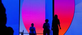 Silhuetter står framför en stor skärm med en livfull gradient från blått till rosa och orange.