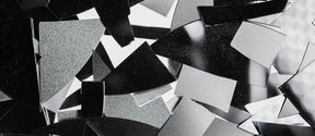 A photograph in black and white, with pieces of materials on a surface. The materials are of different shades of white, grey and black. This is a photo called Structural colours by Eeva Suorlahti.