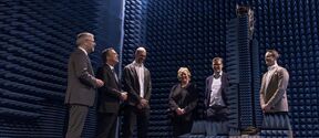 Group of people in a room with blue soundproofing panels, standing around a tall antenna structure.