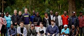 A group of people are posing together outdoors in front of trees and greenery.