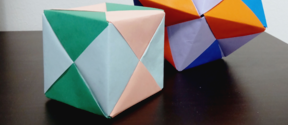 Kaksi geometristä origamia tummalla pöydällä, teksti 'Geometriaa origameilla'.