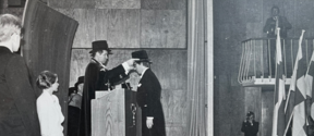 Conferrer Jaakko Honko places the doctoral hat on Promovendi Doctor Jyrki Wallenius. Next to the Conferrer stands Mercury Maiden (nowadays Spirit of Mercury) Sinikka Kaskimies. The photo is from the 1976 Conferment Ceremony. The photograph was taken by the official photographer of the Conferment.