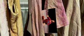 Hanging dyed fabric and a photo of a man. Fabrics are in shades of pink, yellow and beige.