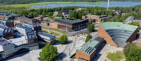 Aerial view of Aalto University campus in Otaniemi, Finland. Modern buildings, green spaces, and a lake in the background.