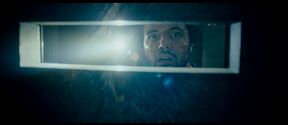 A bright light shines through the window with a rectangular frame, illuminating dust particles in the dark space.
