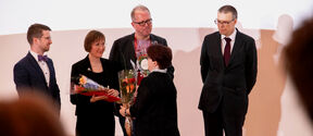 Four awarded individuals dressed in dark clothing receiving bouquets at the academic year's opening ceremony.