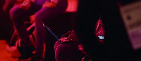 People sitting with laptops and mobile phones in a dimly lit, red-tinged room.