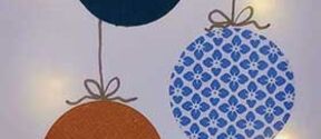 Three hanging ornaments: dark blue, orange, and blue with a floral pattern, each tied with a bow.