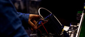 A person in a blue shirt working with a complex electronic device with various coloured wires.
