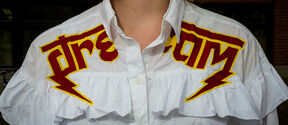 A white shirt with red and yellow embroidery spelling 'dream' and lightning bolts on the shoulders.