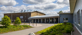 A modern school building with a playground, surrounded by greenery under a partly cloudy sky.