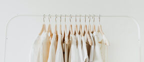 A row of white and beige clothes on wooden hangers on a white clothing rack.