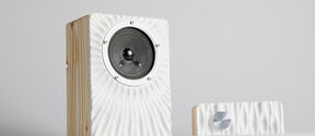 A wooden speaker with a textured white front and a smaller matching device with a round metal button.