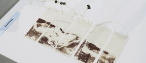 Five rectangular tags with abstract brown prints, connected by strings with black beads, displayed on a white surface.