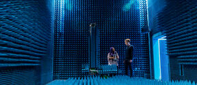 Two people stand in a room with blue, spiked walls and floor, likely an anechoic chamber used for testing acoustics.