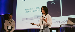 Two people presenting data on Nordic markets. One holds a microphone, the other gestures towards a screen.