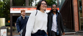 Three people walking outside Aalto University metro station. One wears a white sweater and carries a black bag.