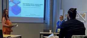 A classroom presentation on geopolymers for greener ceramics. A woman stands near a screen, two people sit at desks.