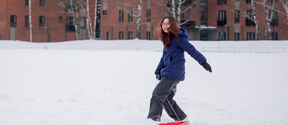 Person in a blue coat pulling a red sled in a snowy area with brick buildings and bare trees in the background.
