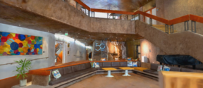 A modern lobby with a large brown sectional sofa, colourful artwork, and a staircase. A '50' logo is on the back wall.