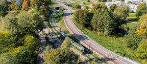 Aerial view of a tram on a curved track surrounded by trees and buildings in a cityscape on a sunny day.