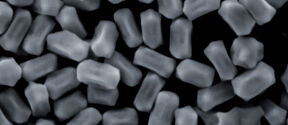 Useita pieniä, suorakulmaisia hiukkasia, joissa on pyöristetyt reunat, harmaana tummalla taustalla.