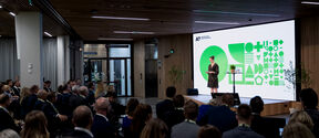 Event at the business school main building. A crowd is watching a presentation on stage.