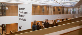 Business School main building. Students standing on stairs having a conversation.