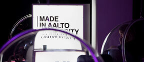 Kyltti lukee 'Made in Aalto University' ja alla iso 'A'. Läpinäkyvät kuplatuolit etualalla.