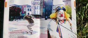An open book showing a skateboarder and a clown against a backdrop of buildings and green grass.