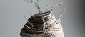 Coiled beige rope sculpture with twisted silver wire branches rising from the top, on a grey background.