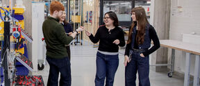 Four students talk in a workshop, surrounded by tools, workbenches and industrial equipment.