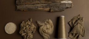 Brown-toned display of wood, pulp, fibre, thread cone and knitted fabric, showing stages from log to textile.