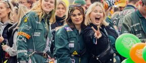 Studenter i gröna overaller på ett livligt utomhusevenemang, ballonger och en gör fredstecken