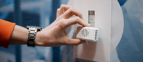 Hand in orange sleeve adjusts small white sensor on wall panel with scale