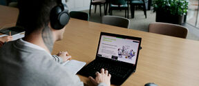 Person with headphones at a long table studying group discussion slides on a laptop in a modern room