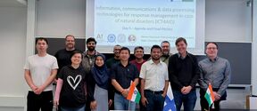 Group of students in a classroom, standing before a disaster response slide, with Finnish and Indian flags on table