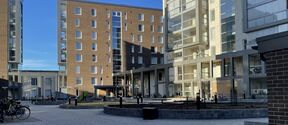 Nykyaikainen tiili- ja lasikerrostalojen piha, laatoitettu aukio, polkupyöriä ja matalia istutusalueita