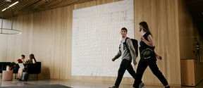 Two students walk through a modern wood-panelled lobby, while two others sit chatting on black sofas