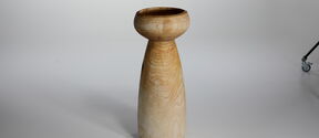 Tall, light brown wooden pedestal or vase with rounded top, standing on a plain light background
