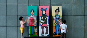 Two children play with bright cartoon panels on a grey tiled wall, spinning sections to mix the figures.