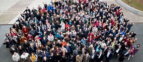 Large diverse crowd outdoors, looking up and waving, dressed in colourful winter clothes