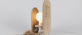 Minimalist table lamp with round bulb and two beige panels, beside dried grass on a light background