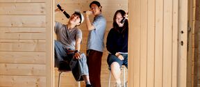 Three young people on stools in a wooden room, holding microphones and posing playfully