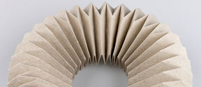 A folded origami structure with symmetrical pleats curves across a grey background.