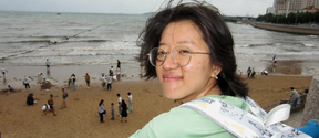 Smiling person in glasses on a seaside pier, crowded sandy beach and city skyline in the background