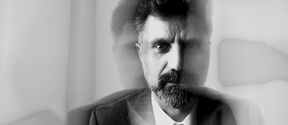 Black and white double exposure of a bearded man in a suit and tie, looking serious at the camera